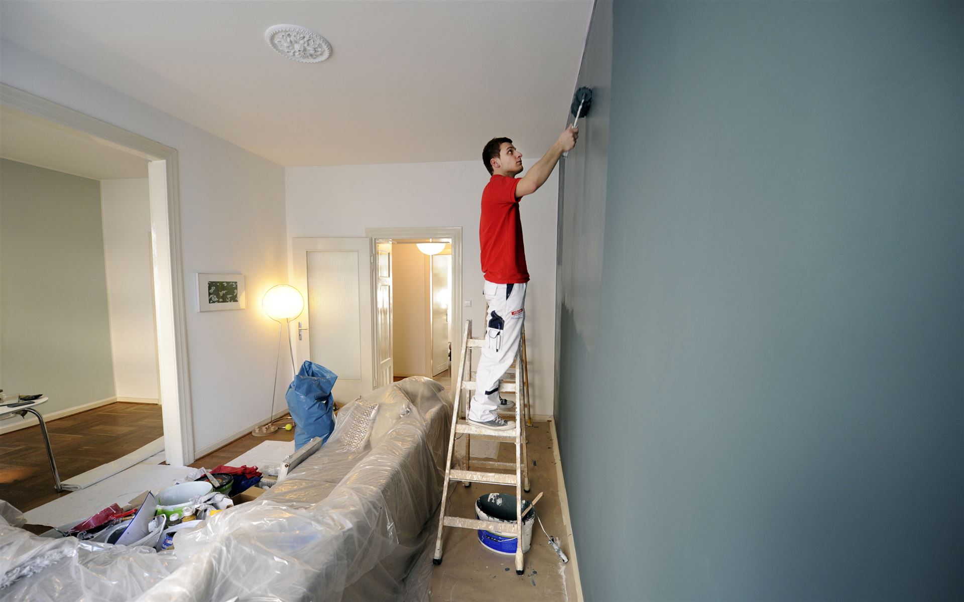 Maler streicht eine Wohnzimmerwand mit einer Farbrolle — Malerarbeiten in Rostock